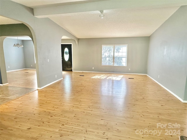 foyer with lofted ceiling with beams, light wood-type flooring, a chandelier, and a textured ceiling