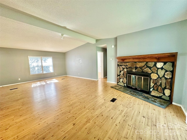 living room featuring vaulted ceiling with beams, light hardwood / wood-style flooring, a textured ceiling, and a stone fireplace