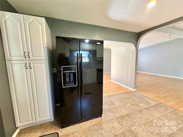 kitchen with arched walkways, black fridge with ice dispenser, white cabinetry, baseboards, and light wood finished floors