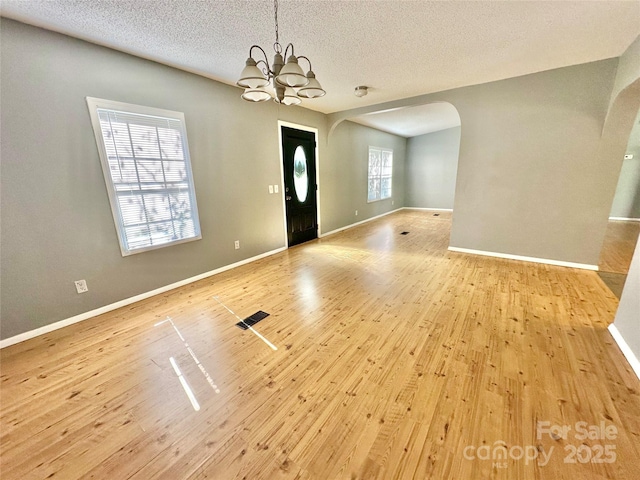 interior space featuring arched walkways, a chandelier, light wood-style flooring, and baseboards