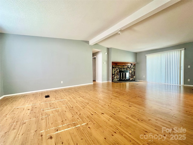 unfurnished living room featuring lofted ceiling with beams, a textured ceiling, a stone fireplace, baseboards, and wood-type flooring