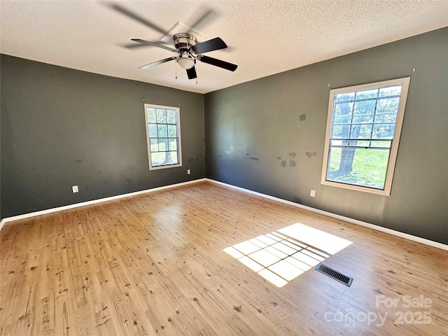 unfurnished room with a textured ceiling, ceiling fan, wood finished floors, visible vents, and baseboards