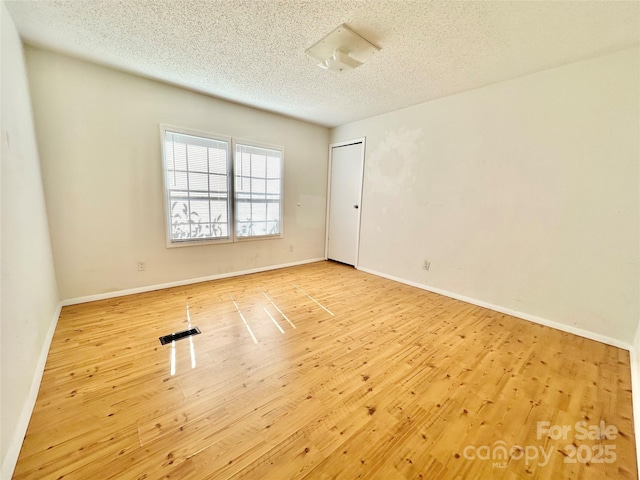 spare room with a textured ceiling, wood finished floors, visible vents, and baseboards