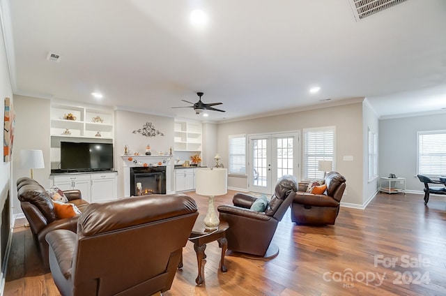 living room with hardwood / wood-style floors, ceiling fan, built in shelves, crown molding, and french doors