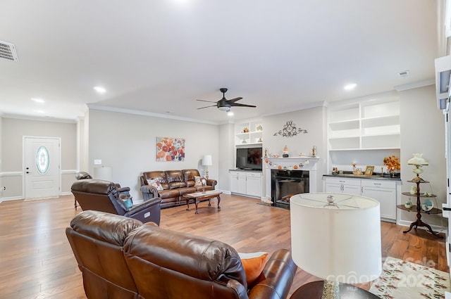 living room with crown molding, built in features, light wood-type flooring, and ceiling fan