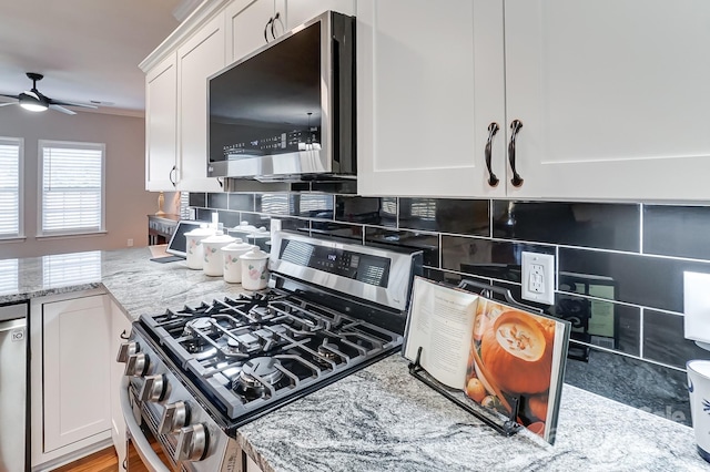 kitchen with tasteful backsplash, appliances with stainless steel finishes, white cabinetry, ceiling fan, and light stone counters