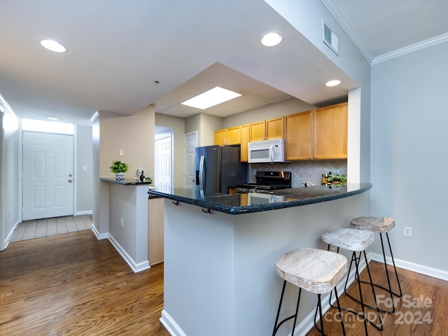 kitchen featuring kitchen peninsula, hardwood / wood-style floors, stainless steel appliances, and a kitchen bar