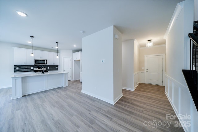 kitchen featuring appliances with stainless steel finishes, pendant lighting, white cabinets, backsplash, and light hardwood / wood-style flooring