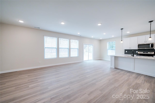 kitchen with appliances with stainless steel finishes, pendant lighting, white cabinetry, sink, and backsplash