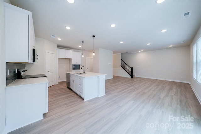 kitchen with pendant lighting, sink, stainless steel appliances, an island with sink, and white cabinets