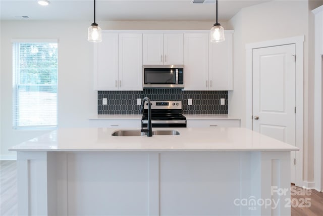 kitchen featuring appliances with stainless steel finishes, a center island with sink, and decorative light fixtures