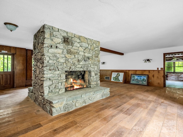 unfurnished living room with wood-type flooring, a stone fireplace, a textured ceiling, and wood walls