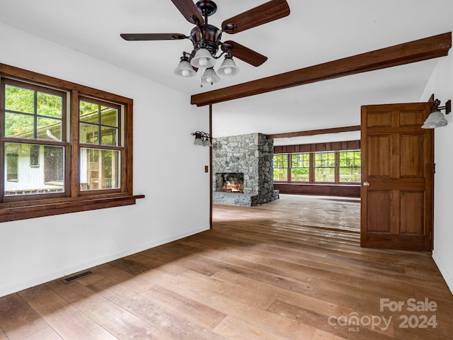 unfurnished living room featuring beamed ceiling, ceiling fan, a stone fireplace, and wood-type flooring