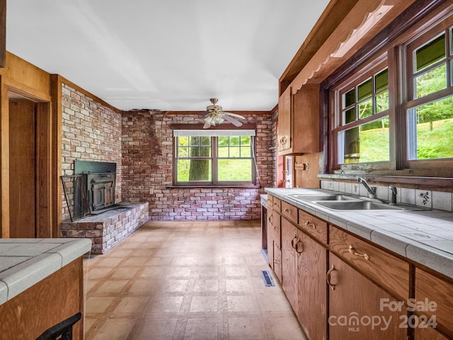 kitchen with a wealth of natural light, sink, tile countertops, and brick wall