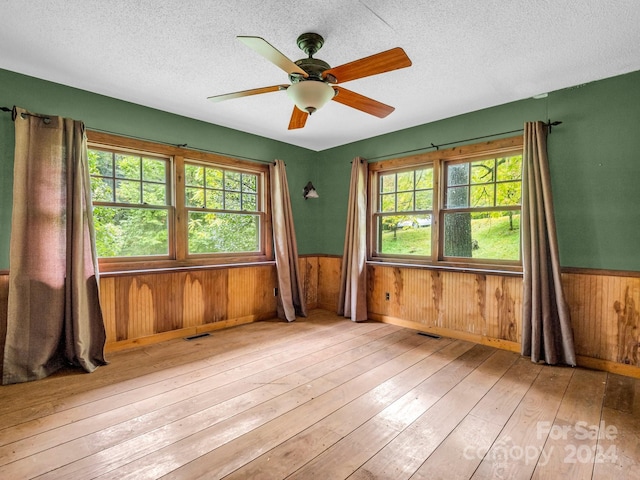 empty room featuring a textured ceiling, ceiling fan, wood walls, and light hardwood / wood-style flooring