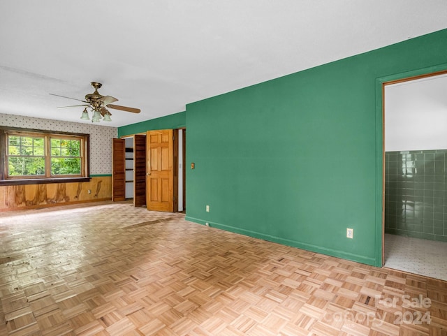 unfurnished living room featuring wood walls, light parquet floors, and ceiling fan