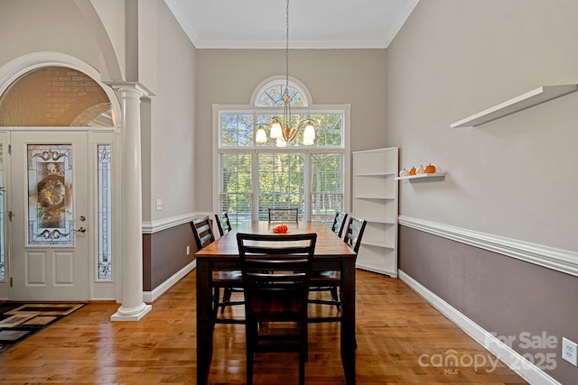 dining space with ornate columns, wood-type flooring, ornamental molding, and an inviting chandelier