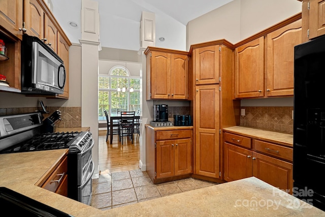 kitchen featuring stainless steel gas range, lofted ceiling, decorative backsplash, black fridge with ice dispenser, and light tile patterned floors