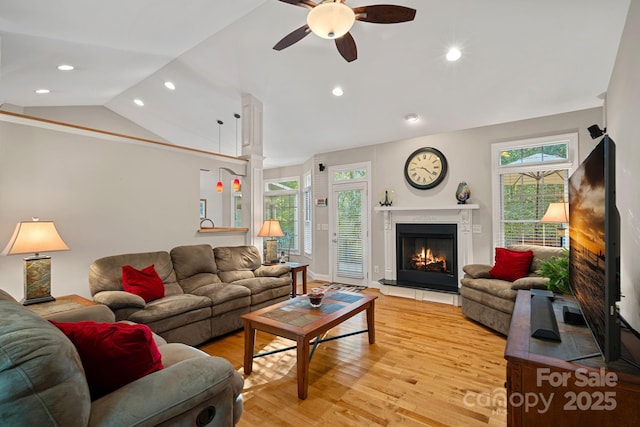 living room featuring a tile fireplace, a healthy amount of sunlight, lofted ceiling, and light wood-type flooring