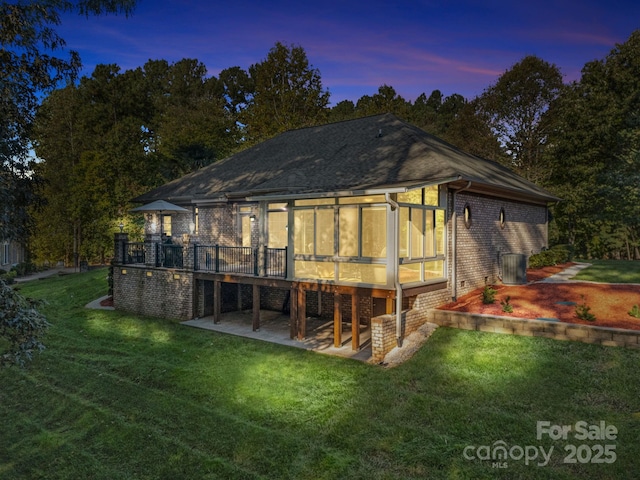 back house at dusk with a lawn and a sunroom