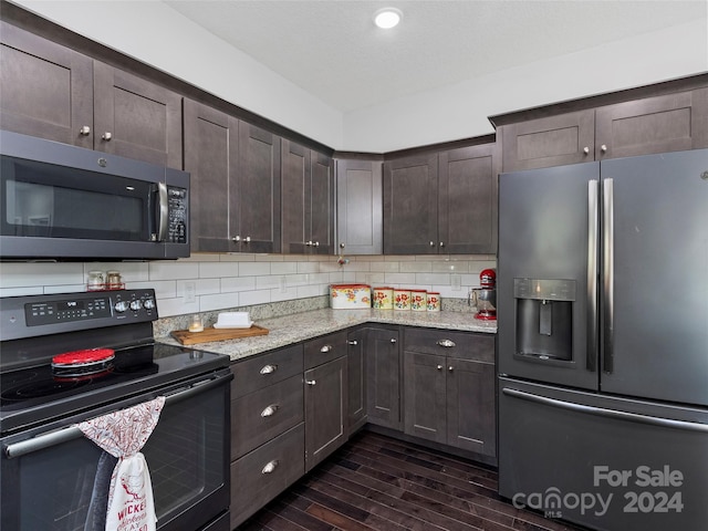 kitchen with tasteful backsplash, dark brown cabinets, appliances with stainless steel finishes, dark hardwood / wood-style floors, and light stone countertops