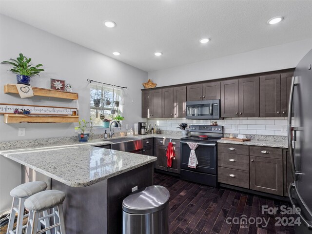 kitchen with a breakfast bar area, dark brown cabinets, stainless steel appliances, light stone countertops, and dark hardwood / wood-style floors