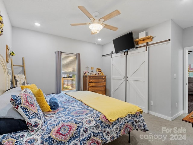 carpeted bedroom with a barn door and ceiling fan