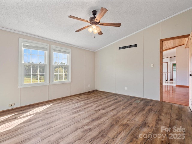 empty room with vaulted ceiling, ornamental molding, a ceiling fan, and wood finished floors