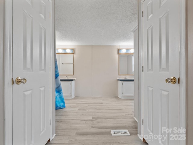 corridor featuring visible vents, a textured ceiling, and light wood finished floors