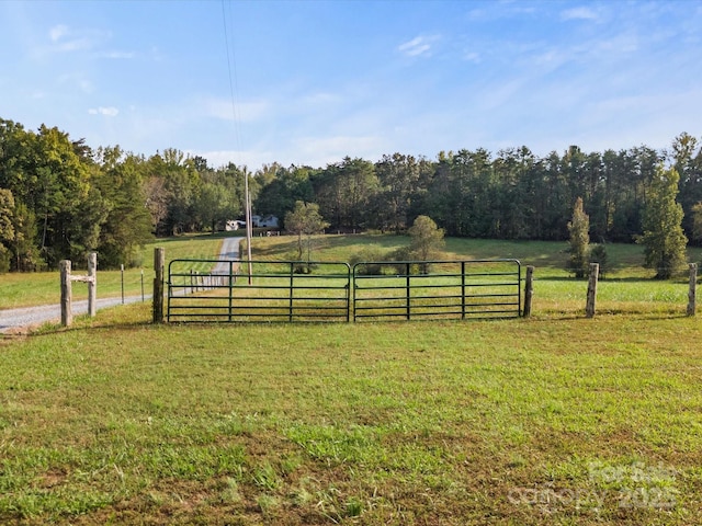 view of yard with a rural view, a view of trees, fence, and a gate