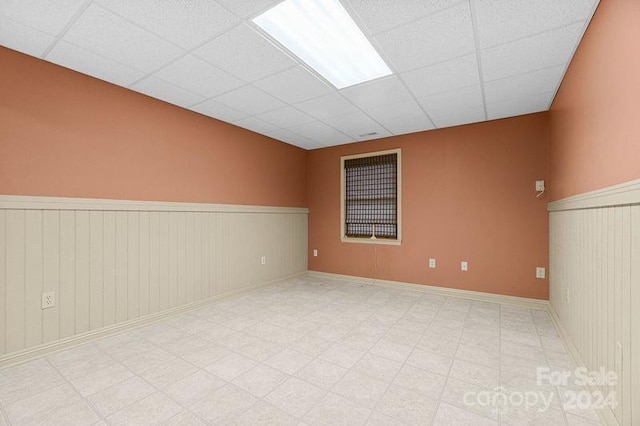 empty room featuring a paneled ceiling and wooden walls