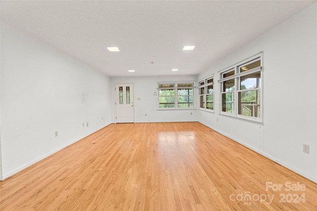 empty room with a textured ceiling and light hardwood / wood-style flooring