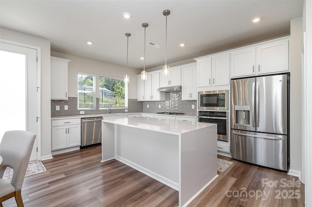 kitchen featuring stainless steel appliances, white cabinets, a center island, and decorative light fixtures