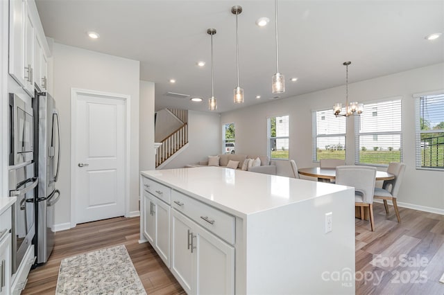 kitchen featuring stainless steel appliances, decorative light fixtures, white cabinetry, light hardwood / wood-style flooring, and a kitchen island