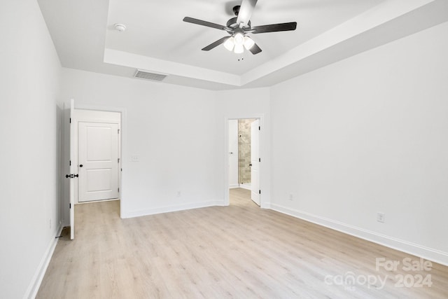 empty room with ceiling fan, light hardwood / wood-style floors, and a raised ceiling