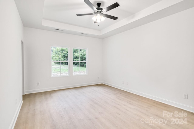 spare room featuring light hardwood / wood-style floors, a tray ceiling, and ceiling fan