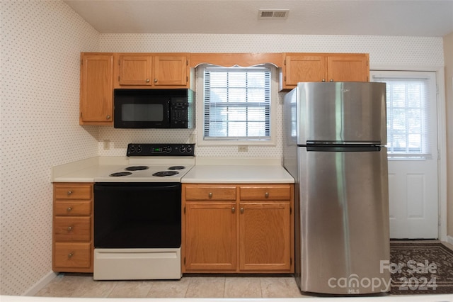 kitchen with light tile patterned flooring, a wealth of natural light, stainless steel refrigerator, and electric range