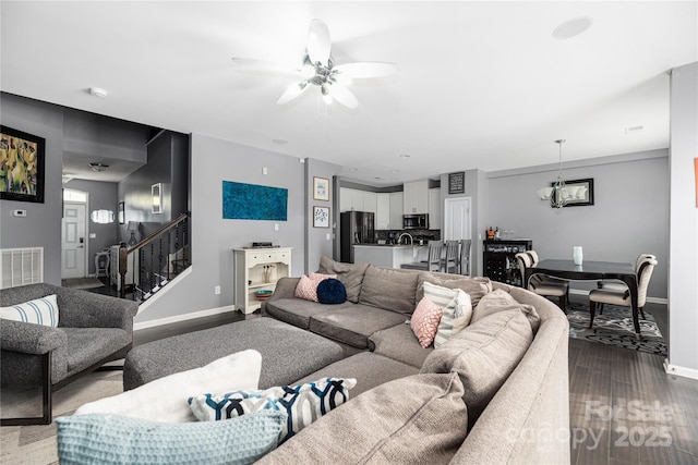 living room with baseboards, visible vents, stairway, wood finished floors, and ceiling fan with notable chandelier