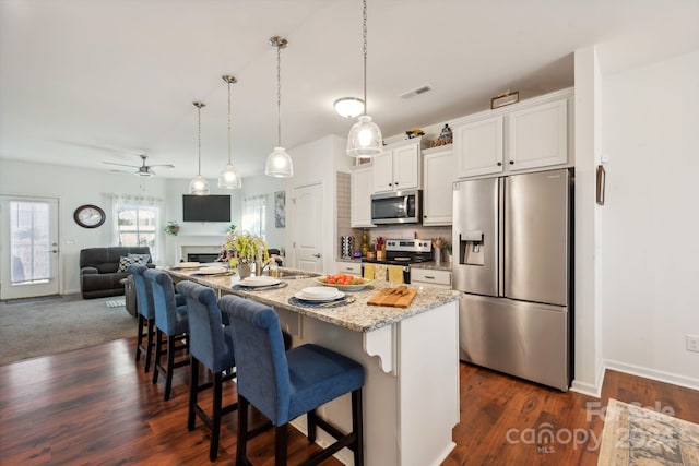 kitchen featuring ceiling fan, an island with sink, a breakfast bar area, white cabinets, and appliances with stainless steel finishes