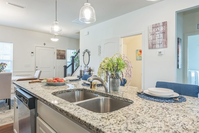 kitchen with sink, stainless steel dishwasher, light stone countertops, decorative light fixtures, and wood-type flooring