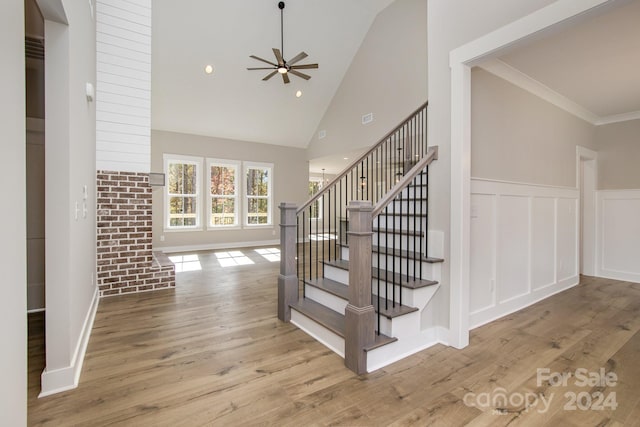 staircase with ceiling fan, hardwood / wood-style flooring, ornamental molding, and high vaulted ceiling