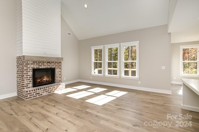 unfurnished living room with light hardwood / wood-style flooring, a fireplace, high vaulted ceiling, and a healthy amount of sunlight