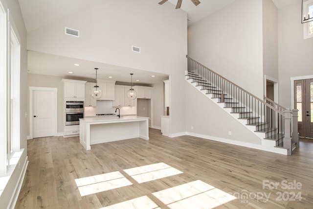 unfurnished living room featuring sink, light hardwood / wood-style flooring, high vaulted ceiling, and ceiling fan