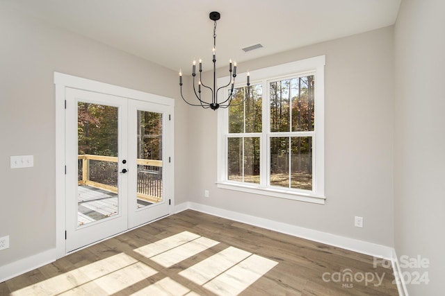 unfurnished dining area featuring french doors, a notable chandelier, plenty of natural light, and hardwood / wood-style floors