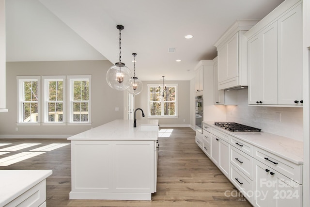 kitchen with an island with sink, white cabinetry, stainless steel appliances, light hardwood / wood-style flooring, and a chandelier