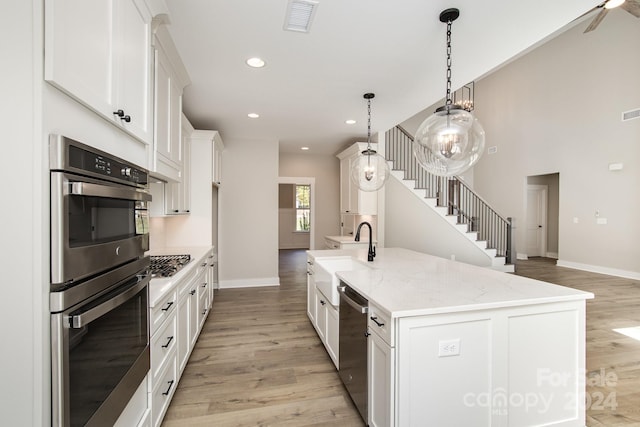 kitchen featuring light hardwood / wood-style flooring, stainless steel appliances, sink, pendant lighting, and white cabinetry