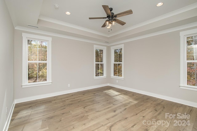 unfurnished room featuring crown molding, ceiling fan, light wood-type flooring, and a raised ceiling