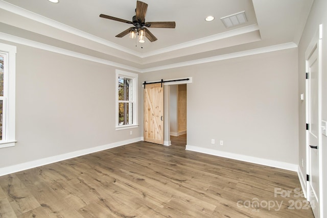 unfurnished bedroom featuring a barn door, a tray ceiling, hardwood / wood-style floors, ceiling fan, and crown molding