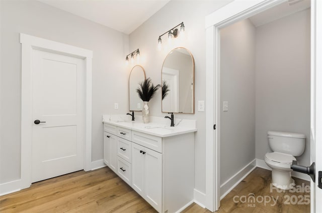 bathroom with wood finished floors, toilet, double vanity, and baseboards