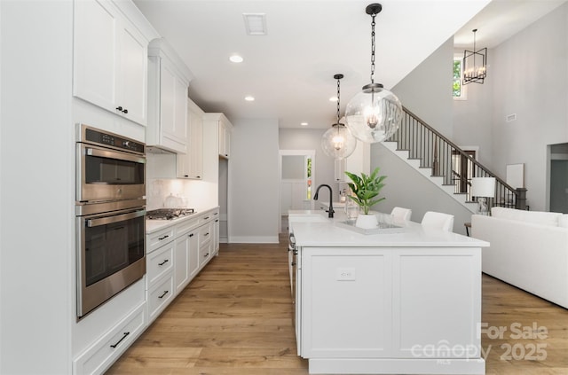 kitchen with a sink, stainless steel appliances, white cabinetry, light countertops, and light wood-style flooring